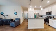 This single-floor residence offers a thoughtfully designed open-concept layout that seamlessly connects the living, dining, and kitchen areas. The kitchen is a standout feature, showcasing crisp white shaker cabinetry, granite countertops, stainless steel appliances including a refrigerator, microwave, and range, and a peninsula with pendant lighting that doubles as a casual dining or prep space. Hardwood-style flooring runs throughout the main living areas, adding warmth and visual continuity.

The living room is bright and inviting, featuring a ceiling fan, large windows with access to an outdoor balcony, and ample space for comfortable seating arrangements. A dedicated dining area adjacent to the kitchen completes the open-concept flow.

The bedrooms are carpeted for comfort and feature large windows that allow natural light to fill each room. The bedrooms are generously sized, offering room for full bedroom furniture arrangements.

The bathroom continues the home's clean aesthetic with white cabinetry, granite countertops, a single vanity with a well-lit mirror, and hardwood-style flooring. Neutral wall tones and consistent finishes throughout the space create a cohesive, modern ambiance that is both functional and visually appealing.