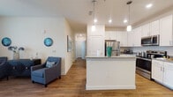This single-floor residence offers a thoughtfully designed open-concept layout that seamlessly connects the living, dining, and kitchen areas. The kitchen is a standout feature, showcasing crisp white shaker cabinetry, granite countertops, stainless steel appliances including a refrigerator, microwave, and range, and a peninsula with pendant lighting that doubles as a casual dining or prep space. Hardwood-style flooring runs throughout the main living areas, adding warmth and visual continuity.

The living room is bright and inviting, featuring a ceiling fan, large windows with access to an outdoor balcony, and ample space for comfortable seating arrangements. A dedicated dining area adjacent to the kitchen completes the open-concept flow.

The bedrooms are carpeted for comfort and feature large windows that allow natural light to fill each room. The bedrooms are generously sized, offering room for full bedroom furniture arrangements.

The bathroom continues the home's clean aesthetic with white cabinetry, granite countertops, a single vanity with a well-lit mirror, and hardwood-style flooring. Neutral wall tones and consistent finishes throughout the space create a cohesive, modern ambiance that is both functional and visually appealing.