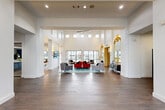 Located at 3100 E Stadium Blvd in Columbia, Missouri, this large-scale amenity facility spans a single floor and offers a comprehensive suite of spaces designed for fitness, productivity, and social engagement. The grand common area greets visitors with soaring double-height ceilings, abundant natural light from clerestory windows, wide-plank hardwood-style flooring, and a curated seating arrangement anchored by bold red and gray upholstered furniture, complemented by a decorative gold-framed mirror.

The facility features two dedicated fitness areas: a large, well-equipped gym with rows of treadmills, strength machines, free weights, and oversized ceiling fans, as well as a secondary functional fitness studio with cardio equipment and open floor space. A stylish library doubles as a conference and study room, appointed with navy walls, a bookshelf-print accent wall, elegant multi-lamp chandeliers, and rows of sleek white tables with modern rolling chairs. Adjacent private study rooms—named "The Houston," "The Stanton," and "The Rivington"—offer glass-walled, individually enclosed workspaces ideal for focused study or meetings. A lounge area with comfortable neutral seating and built-in workstations connects these rooms. "The Joe" kitchen features navy cabinetry, a geometric tile backsplash, stainless steel appliances, and a large island with bar seating, with direct access to an outdoor pool area.
