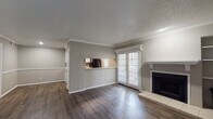 This single-floor residence offers a well-organized layout that balances open communal spaces with private living quarters. The living area serves as the heart of the home, featuring rich dark hardwood-style flooring, crown molding, and a textured ceiling throughout. A tile-surround fireplace with a white mantel anchors one wall, while a set of French doors floods the space with natural light and provides outdoor access. A pass-through opening connects the living area to the kitchen, enhancing the open feel.

The kitchen is thoughtfully designed with white cabinetry, light countertops, a decorative tile backsplash, and a full suite of black appliances, including a refrigerator, range, built-in microwave, and dishwasher. A window above the sink area brings in additional natural light.

The bedroom is generously sized, finished with plush carpeting, a ceiling fan with light fixture, and a window with blinds. The adjacent bathroom features a wide vanity with a light countertop, a large mirror, and hardwood-style flooring, leading to a separate wet area with a bathtub and shower combination, plus access to a walk-in closet.