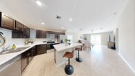 Located in the Osprey community of Fort Pierce, Florida, this single-story home offers a well-designed layout across two bedrooms, two bathrooms, two offices, and a dedicated laundry room. The open-concept kitchen and living area serves as the heart of the home, featuring recessed lighting, light tile flooring, dark espresso cabinetry, stainless steel appliances, and a central island with bar seating — ideal for both cooking and casual dining. The adjoining living room provides a comfortable, airy space with a built-in media wall. The primary bedroom is generously sized, featuring a ceiling fan, a closet with bi-fold doors, and a calm, neutral palette. The second bedroom is equally inviting, with tile flooring and a ceiling fan. Both bathrooms are finished with beige tile surround, a walk-in shower, and dark vanity cabinetry with white countertops. Two dedicated office spaces offer flexibility for work or hobby use, each with ceiling fans and natural light from windows. The laundry room includes wire shelving and appliance hookups. The attached garage offers additional utility and storage space. Outside, the home features a light green stucco exterior, a concrete driveway, and a well-maintained lawn.