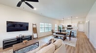 This single-story home offers a thoughtfully designed open-concept floor plan that seamlessly connects the living, dining, and kitchen areas into one bright, cohesive space. Vaulted ceilings and large windows with slatted blinds flood the main living area with natural light, while light-toned hardwood flooring runs throughout, enhancing the airy ambiance. A ceiling fan anchors the living room, which flows effortlessly into the dining area and kitchen.

The kitchen is a standout feature, boasting white shaker cabinets with matte black hardware, a large center island with a farmhouse sink and bar seating, quartz countertops, a subway tile backsplash, and stainless steel appliances including a gas range and French door refrigerator. Pendant lighting adds a modern finishing touch.

The spacious primary bedroom is a private retreat featuring a distinctive tray ceiling, ceiling fan, plush carpet, and multiple windows that invite natural light. Two additional bedrooms provide comfortable accommodations, served by a clean, neutral full bathroom with tile flooring, a tub/shower combo, and a white vanity.

The home also includes two hallways, a closet, and an attached garage with a direct interior access door, offering practical convenience throughout.
