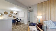 This single-floor residence is thoughtfully designed with a cohesive modern aesthetic that flows throughout each room. Wood-look flooring runs continuously across the living, dining, and bedroom areas, lending warmth and visual continuity to the space.

The living room serves as a focal point, featuring a striking vertical wood-plank accent wall that adds texture and depth. A ceiling fan overhead and glass-paned doors invite natural light while offering a view of mature trees outside, creating a relaxed, airy ambiance.

Adjacent to the living area, the dining space is defined by a drum pendant light and an accent wall adorned with a cluster of sunburst mirrors, giving the area a bold, decorative character.

The galley-style kitchen is efficiently arranged with grey cabinetry, white countertops, a tile backsplash, and stainless steel appliances, providing ample workspace and storage.

Two bedrooms offer distinct personalities — one features a dramatic navy accent wall with a ceiling fan and natural window light, while the other is more neutral and serene. Both connect conveniently to the rest of the unit.

The bathroom is well-equipped with grey cabinetry, a wide vanity mirror, and a tall storage cabinet, balancing functionality with a clean, contemporary finish.