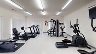 Located on Williamsburg Drive in Augusta, Georgia, this single-floor fitness center offers a comprehensive range of exercise equipment within a bright, clean environment. The space is organized to accommodate both cardiovascular and strength training needs, making it a versatile facility for users with varying fitness goals.

The cardio area is equipped with multiple treadmills and an elliptical machine, each positioned in front of wall-mounted flat-screen televisions, providing entertainment during workouts. Fluorescent lighting fixtures installed across the ceiling ensure consistent, even illumination throughout the space. The light-colored vinyl flooring adds to the overall brightness of the room.

On the strength training side, the facility includes a multi-function cable and weight machine, a flat workout bench, a recumbent bike, and a dumbbell rack stocked with free weights. A wall-mounted sanitizing dispenser and a built-in utility sink near the exit door support hygiene and cleanliness. Vertical blinds cover large windows along one wall, allowing natural light to filter in while maintaining privacy.

The layout is open and uncluttered, providing ample floor space for movement between equipment. The space maintains a functional, no-frills aesthetic suited to an active community fitness environment.