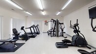 Located on Williamsburg Drive in Augusta, Georgia, this single-floor fitness center offers a comprehensive range of exercise equipment within a bright, clean environment. The space is organized to accommodate both cardiovascular and strength training needs, making it a versatile facility for users with varying fitness goals.

The cardio area is equipped with multiple treadmills and an elliptical machine, each positioned in front of wall-mounted flat-screen televisions, providing entertainment during workouts. Fluorescent lighting fixtures installed across the ceiling ensure consistent, even illumination throughout the space. The light-colored vinyl flooring adds to the overall brightness of the room.

On the strength training side, the facility includes a multi-function cable and weight machine, a flat workout bench, a recumbent bike, and a dumbbell rack stocked with free weights. A wall-mounted sanitizing dispenser and a built-in utility sink near the exit door support hygiene and cleanliness. Vertical blinds cover large windows along one wall, allowing natural light to filter in while maintaining privacy.

The layout is open and uncluttered, providing ample floor space for movement between equipment. The space maintains a functional, no-frills aesthetic suited to an active community fitness environment.