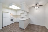 Located at 1815 North Broadway in Escondido, CA, this two-bedroom, two-bathroom residence offers a well-organized single-floor layout with a bright, functional design. The open-concept living, dining, and kitchen area forms the heart of the home, with light wood-look flooring tying the spaces together seamlessly. The kitchen is well-appointed with white cabinetry, light countertops featuring a peninsula, a full suite of white appliances including a dishwasher, and a distinctive skylight that floods the space with natural light. The living area features neutral carpet, a ceiling fan, and a sliding glass door that opens to a private balcony overlooking lush greenery. Both bedrooms are carpeted and include ceiling fans and generous closet space — with six closets distributed throughout the home. The spacious primary bedroom receives natural light through a large window. The two bathrooms are clean and functional: one features a walk-in shower with wood-look flooring and a vanity with a wide mirror, while the other offers a full tub-shower combination. Wall-mounted air conditioning units provide climate control. The overall ambiance is light, neutral, and move-in ready.
