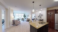 This thoughtfully designed single-floor residence offers an open-concept layout that seamlessly connects the kitchen, dining, and living areas, creating a bright and welcoming atmosphere. The kitchen is a standout feature, showcasing rich dark cabinetry, granite countertops, stainless steel appliances including a refrigerator, electric range, and built-in microwave, as well as hardwood flooring and a peninsula with pendant lighting that overlooks the main living space. The expansive living room is anchored by a tile-surround fireplace with a mounted flat-screen television above, plush carpeting, and large windows that invite abundant natural light. Two well-proportioned bedrooms offer comfortable retreats, each with carpeted floors and ample closet space. One bedroom features a window with outdoor views and direct access to a full en-suite bathroom appointed with dark cabinetry, a dual-sink vanity, and a glass-enclosed shower. A second full bathroom includes a soaking tub with a shower and built-in shelving. The dedicated in-unit laundry room is equipped with a full-size washer and dryer alongside rich wood cabinetry for added storage. Throughout, the residence maintains a cohesive, neutral palette that enhances its sense of space and refinement.