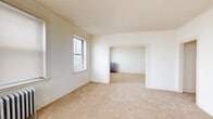 Located at 7447 S South Shore Dr in Chicago's South Shore neighborhood, this single-floor unit offers a well-defined layout with multiple interconnected rooms. The interior is characterized by neutral white walls, textured ceilings, and warm beige carpeting throughout the living and sleeping areas, creating a clean and functional atmosphere.

The living spaces are generously proportioned, with multiple windows fitted with blinds that allow for adjustable natural light. Classic cast-iron radiators are present throughout, providing consistent radiant heat and serving as a nod to the building's architectural heritage. Detailed door and window trim adds a traditional character to each room.

A central hallway connects the rooms and leads to the front entry door, providing a clear and practical flow through the unit. Wall-mounted light fixtures illuminate the corridors efficiently.

The kitchen is equipped with white cabinetry featuring wood trim accents, a stainless steel refrigerator, a stainless steel gas range, and a built-in shelving nook. Tile-pattern flooring and a window above the work area complete the functional kitchen space.

The bathroom features a classic soaking tub with a shower, white tile surround, a vanity with mirror, terrazzo-style flooring, a window for natural light, and a radiator for warmth. Additional closet and storage space is accessible throughout the unit.