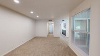 Located at 903 S Euless Main St in Euless, Texas, this single-story home offers four bedrooms and two full bathrooms within a compact, efficiently arranged floor plan. The layout connects key living spaces through two hallways, creating a straightforward flow from the entrance through the home.

The living room is finished with plush wall-to-wall carpeting and features recessed lighting overhead, a large window fitted with blinds that invites natural light, and direct sightlines to both the kitchen and the hallway leading to the bedrooms. The galley-style kitchen is a notable feature, showcasing dark cabinetry with modern hardware, white countertops, a tiled backsplash, a double-basin sink, and black appliances including a refrigerator and electric range. Light wood-look flooring runs through the kitchen, complementing the clean, contemporary aesthetic.

The bedrooms are carpeted and neutral in tone, with windows providing natural light and outdoor views. The primary bedroom includes a ceiling fan with integrated lighting. Both bathrooms feature tub-shower combinations with white tile surrounds and brushed nickel fixtures. Throughout the home, a consistent palette of white walls and neutral flooring creates a clean, move-in ready environment.