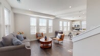 This two-floor residence is designed with a clean, contemporary aesthetic that prioritizes natural light and functional flow throughout. The main level showcases an open-concept layout where the living, dining, and kitchen areas connect seamlessly. Rich, dark hardwood flooring anchors the space, complementing neutral gray walls and white trim. The living area is lined with multiple large windows dressed with white blinds, allowing abundant natural light to pour in from multiple directions.

The kitchen is well-equipped with white shaker-style cabinetry, stainless steel appliances including a refrigerator, range, and microwave, and a peninsula with a white countertop that accommodates bar-height seating. Pendant lights hang above the peninsula, adding a refined touch. A dedicated dining nook nearby features additional window coverage, creating an airy setting for meals.

The upper floor hosts generously sized bedrooms carpeted for comfort, each featuring ceiling fans, multiple windows with outdoor views, and ample closet space. The primary bedroom includes a built-in closet with shelving. Two full bathrooms serve the home — one with a tub-shower combination and another with a walk-in shower — both finished with white vanities and hardwood-style flooring, maintaining the home's cohesive, polished character throughout.