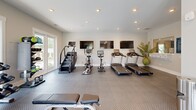 Located at 50 Newport Blvd in Port Wentworth, Georgia, this well-appointed fitness center offers a dedicated exercise space designed to support a comprehensive workout routine. The room features durable diamond-plate rubber flooring throughout, recessed lighting in the white ceiling, and neutral-toned walls that create a clean, focused environment.

Cardio equipment is a highlight of the space, with multiple treadmills, a stair climber, an elliptical, and a stationary bike arranged along one wall — each paired with a wall-mounted flat-screen television for entertainment during workouts. A multi-functional cable machine and a full rack of dumbbells provide ample options for strength training.

Natural light fills the room through multiple sets of large French doors and windows, offering views of the outdoor pool area and surrounding greenery — creating an inviting, airy atmosphere. A dual-level water fountain station with a stainless steel waste bin is conveniently positioned along the wall, ensuring easy hydration access. Decorative touches, including a large blue wall canvas and potted plants, add a welcoming aesthetic to the functional space. The fitness center is a practical and well-equipped amenity for residents seeking convenient access to quality exercise facilities.