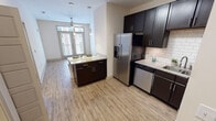Located at 300 State St in the heart of downtown Knoxville, Tennessee, this single-floor residence offers a well-appointed layout with modern finishes and thoughtful design details throughout. The kitchen serves as a focal point of the space, showcasing rich dark cabinetry, light granite countertops, a classic white subway tile backsplash, and a full suite of stainless steel appliances including a side-by-side refrigerator with ice and water dispenser, dishwasher, microwave, and range. A center island provides additional prep and seating space, while pendant lighting above adds a refined touch. Light-toned wood-style flooring runs through the kitchen and living areas, creating a bright and cohesive aesthetic. Natural light filters into the living area through large windows and glass doors fitted with blinds. The bedroom is carpeted for comfort, features a ceiling fan, and includes a window with a view of the surrounding neighborhood. The bathroom is finished with large-format tile flooring, dark vanity cabinetry with granite countertops, and a full tub-shower combination with white subway tile surround. The overall design balances contemporary style with functional living in a prime Knoxville location.