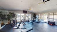Located at 2660 Alpine Blvd in Alpine, California, this single-story fitness center offers a well-appointed workout facility designed to support a comprehensive exercise routine. The space is divided into distinct functional zones, providing room for both cardio training and strength work without feeling cramped.

The main cardio area is bright and airy, benefiting from an abundance of natural light streaming through multiple sets of French doors and large windows that look out onto a neighboring pool area and surrounding greenery. Ceiling fans overhead help maintain a comfortable environment during workouts. Equipment in this zone includes treadmills, an elliptical trainer, a stationary cycle, and a rowing machine, alongside adjustable weight benches. A wall-mounted flat-screen television adds convenience for longer sessions. Large mirrors along one wall further enhance the sense of openness.

A separate strength training area features a cable/functional trainer machine, a full rack of dumbbells, a medicine ball, and additional benches. This section is distinguished by a dramatic floor-to-ceiling mountain landscape mural, adding a bold visual element to the space. Durable rubberized flooring throughout the entire facility provides safety and sound absorption.

Additional access points include a side door leading to a parking area, making entry and exit convenient from multiple directions. Decorative potted plants are placed throughout, contributing to a welcoming and refreshing atmosphere.