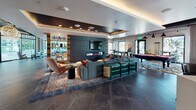 Located at 1331 N Cahuenga Blvd in the heart of Hollywood, this single-floor amenity space is a thoughtfully designed communal hub that blends contemporary style with eclectic, arts-inspired character. The grand lobby entry sets the tone immediately, featuring dramatic globe chandeliers, large-format dark tile flooring, floor-to-ceiling glass walls that flood the space with natural light, and lush potted greenery that softens the modern aesthetic.

The main lounge area is anchored by a bold feature wall clad in dark paneling with a built-in fireplace and mounted flat-screen TV. Plush sectional seating, colorful accent chairs, and patterned area rugs create an inviting social environment. Adjacent to the lounge, a game room offers a pool table, shuffleboard, high-top seating, and large windows with views of the surrounding cityscape, all beneath an exposed industrial ceiling with track lighting.

A dedicated co-working zone provides a round conference table beneath oversized teal pendant lamps, designed for collaborative work or private meetings. The kitchenette features clean-lined cabinetry, quartz countertops, beverage refrigerators, and wall-mounted TVs. Curated artwork — including bold large-scale paintings and a cassette tape wall installation — lends the space a distinctly creative, LA-inspired identity. Stylishly appointed restrooms complete this well-rounded amenity floor.