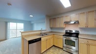This single-floor unit offers a practical and comfortable layout designed to maximize functionality. The kitchen is a standout feature, outfitted with light maple cabinetry, ample upper and lower storage, neutral laminate countertops, and a full suite of stainless steel appliances including a refrigerator, electric range, dishwasher, and a range hood. Stone-look tile flooring runs throughout the kitchen and entry area, adding durability and a clean aesthetic. A breakfast bar-style counter separates the kitchen from the open living area, which features plush wall-to-wall carpeting and recessed lighting that creates a bright, welcoming atmosphere. The living space flows seamlessly to adjacent areas, including a well-lit bathroom with a clean, white tub-shower surround, and a closet space for additional storage. The bedroom is generously sized with soft carpeting and features a built-in closet organizer with shelving and drawers for ample organization. A sliding glass door opens to a private balcony offering open views of the surrounding cityscape, allowing abundant natural light to fill the room. The entry door is equipped with a keypad access system, adding a layer of modern convenience and security to the unit overall.