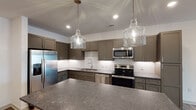 Located in Grandover Village, Greensboro, NC, this thoughtfully designed single-floor residence offers a seamless open-concept layout that connects the living, dining, and kitchen areas. The kitchen is a standout feature, showcasing taupe shaker-style cabinetry, stone countertops, a classic white subway tile backsplash, and a full suite of stainless steel appliances including a refrigerator with ice maker, electric range, microwave, and dishwasher. Elegant glass pendant lights illuminate a spacious island, making it an ideal space for both cooking and entertaining. Wood-look plank flooring flows throughout the main living areas, lending warmth and continuity to the space. Bedrooms are finished with plush carpeting and ceiling fans, with windows providing natural light and outdoor views. The bathroom features stone-look tile flooring, granite-topped vanity cabinetry, and a full tub-shower combination with white tile surround, along with access to a walk-in closet with built-in shelving. A dedicated laundry room houses a full-size washer and dryer. Clean white walls, recessed lighting, and modern fixtures throughout contribute to a bright, contemporary ambiance well-suited to comfortable everyday living.