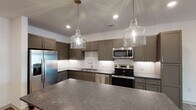 Located in Grandover Village, Greensboro, NC, this thoughtfully designed single-floor residence offers a seamless open-concept layout that connects the living, dining, and kitchen areas. The kitchen is a standout feature, showcasing taupe shaker-style cabinetry, stone countertops, a classic white subway tile backsplash, and a full suite of stainless steel appliances including a refrigerator with ice maker, electric range, microwave, and dishwasher. Elegant glass pendant lights illuminate a spacious island, making it an ideal space for both cooking and entertaining. Wood-look plank flooring flows throughout the main living areas, lending warmth and continuity to the space. Bedrooms are finished with plush carpeting and ceiling fans, with windows providing natural light and outdoor views. The bathroom features stone-look tile flooring, granite-topped vanity cabinetry, and a full tub-shower combination with white tile surround, along with access to a walk-in closet with built-in shelving. A dedicated laundry room houses a full-size washer and dryer. Clean white walls, recessed lighting, and modern fixtures throughout contribute to a bright, contemporary ambiance well-suited to comfortable everyday living.