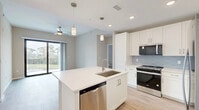 Located in Bonita Springs, FL, this well-appointed 2-bedroom, 2-bathroom residence offers a thoughtfully designed single-floor layout. The open-concept living area seamlessly connects the kitchen, dining, and living spaces, all finished with light wood-look flooring that enhances the bright, airy atmosphere. The kitchen is a standout feature, showcasing white shaker cabinetry, light blue subway tile backsplash, quartz countertops, stainless steel appliances, and a central island with an undermount sink and built-in dishwasher — ideal for both cooking and entertaining. Sliding glass doors lead to a private patio, offering peaceful views of the surrounding Florida landscape. The generously sized primary bedroom features its own access to the outdoors, a ceiling fan, and a walk-in closet with wire shelving throughout. The second bedroom is carpeted, filled with natural light from a large window, and includes its own closet. Both bathrooms are finished with white vanities, quartz countertops, and walk-in showers. Additional highlights include an in-unit laundry area, a hallway connecting all rooms efficiently, and a consistent neutral color palette that lends the home a clean, contemporary feel throughout.