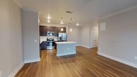 Located on Teel Parkway in Frisco, Texas, this single-story unit offers a well-designed, open-concept layout that seamlessly connects the kitchen and living areas. Rich hardwood-style flooring runs throughout the main living spaces, complemented by crown molding and neutral gray walls that create a clean, cohesive aesthetic.

The kitchen is a standout feature, showcasing dark espresso cabinetry extending to the ceiling for ample storage, a full suite of stainless steel appliances including a French door refrigerator, built-in microwave, range, and dishwasher. A large center island with a crisp white countertop provides additional workspace and serves as a natural gathering point. Pendant lighting above the island adds a refined touch.

The living area is generously proportioned, featuring a ceiling fan and French doors that open to an outdoor space, allowing natural light to fill the room. Bedrooms are finished with plush carpeting and ceiling fans, offering comfortable, quiet retreats. Windows with blinds provide natural light and privacy.

The bathroom includes a soaking tub and shower combination with stylish vertical tile surround, while adjacent closet space adds practical storage. Overall, the space balances functional design with contemporary finishes throughout.
