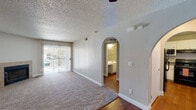 This single-floor residence combines functional design with comfortable living across a well-organized layout. The main living area is carpeted and features a textured popcorn ceiling, a ceiling fan, and a sliding glass door that opens to an outdoor balcony, allowing natural light to fill the space. Distinctive arched doorways add a subtle architectural character, connecting the main living area to adjacent rooms.

The kitchen is efficiently arranged in a U-shaped configuration, equipped with white cabinetry, gray countertops, and black appliances including a gas range, microwave, refrigerator, and dishwasher. Warm hardwood-style flooring runs throughout the kitchen and extends into other areas of the unit.

Two bathrooms serve the residence, each featuring white vanity cabinetry, elongated countertops, large mirrors, and hardwood-style flooring. One bathroom includes a shower-tub combination, while the other is appointed with a walk-in shower enclosed by a glass door.

The bedrooms are carpeted and bright, with one room featuring a ceiling fan with a light fixture and a textured ceiling. Additional rooms offer neutral wall tones and windows dressed with blinds, providing privacy and natural light. The overall ambiance is clean, neutral, and move-in ready.