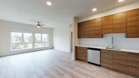 Unit 707 at 3214 Broadway in Everett, Washington offers a thoughtfully designed single-floor layout with a clean, contemporary aesthetic throughout. Light-toned luxury vinyl plank flooring flows seamlessly across every room, complementing the crisp white walls and recessed lighting that keep the space bright and airy.

The open-concept living and kitchen area serves as the heart of the unit. The kitchen is outfitted with flat-front walnut-toned cabinetry extending to the ceiling, white quartz countertops, and a full suite of stainless steel appliances including a refrigerator, electric range, over-the-range microwave, and dishwasher. A ceiling fan in the living area adds comfort, while large windows frame neighborhood views and fill the space with natural light.

The bedroom features multiple windows, including a wide horizontal clerestory window alongside a larger view window that offers elevated cityscape views of Everett — a standout feature of this upper-floor unit.

The bathroom is well-appointed with a walnut-accented vanity, white countertop, and a full soaking tub with shower. A dedicated in-unit laundry closet with a stacked washer and dryer provides added convenience. The overall ambiance is modern and move-in ready, with neutral tones and quality finishes throughout.