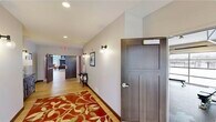 This thoughtfully designed single-floor amenity space offers a comprehensive suite of shared facilities across a generous footprint. The layout is connected by a welcoming corridor featuring warm hardwood flooring, bold patterned area rugs, dark-paneled doors, and elegant globe wall sconces that set an inviting tone throughout.

The community lounge is a standout architectural highlight, boasting soaring two-story ceilings lined with floor-to-ceiling windows that flood the space with natural light and offer expansive outdoor views. A sleek, dark tile fireplace serves as a dramatic focal point, complemented by rich hardwood floors and carefully curated furnishings, including a pool table and flexible seating arrangements.

Adjacent to the lounge, the community kitchen is well-equipped with cream cabinetry, dark stone countertops, a tiled backsplash, stainless steel appliances, and a large island with bar seating. A connected dining area features bold terracotta-red accent walls, large windows with outdoor views, and a spacious dining table ideal for group gatherings.

The fitness center is fully outfitted with cardio machines, a rowing machine, a weight bench, a full dumbbell rack, and a glass garage door that brings in natural light. Mirrors, rubberized flooring, and an organized storage area complete this dedicated wellness space. Throughout, the design blends modern finishes with warm, energetic accents.