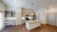 This single-floor residence in Waxahachie, TX offers a thoughtfully designed open layout with modern finishes throughout. The kitchen serves as a central highlight, anchored by a substantial island with speckled granite countertops and an undermount stainless steel sink. Warm pendant lighting illuminates the space, while gray shaker-style cabinetry, a white subway tile backsplash, and a full suite of stainless steel appliances — including a refrigerator, range, and over-the-range microwave — complete the polished look. An adjacent built-in shelving and desk area adds functional versatility to the open living space.

Rich wood-look flooring flows consistently throughout the main areas and bedrooms, contributing to a cohesive and contemporary feel. The bedrooms are well-proportioned, each featuring ceiling fans, window blinds for natural light control, and access to closet space. One bedroom notably includes a walk-in closet with built-in shelving alongside a separate bathroom entry.

The bathroom is finished with marble-style tile surrounding the tub and shower, a granite-topped vanity with an undermount sink, brushed nickel fixtures, and a framed mirror — delivering a clean, upscale aesthetic. Recessed lighting and neutral wall tones throughout the unit create a bright, welcoming ambiance.