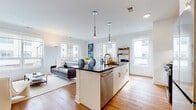This contemporary single-floor residence offers a thoughtfully designed open-concept layout that seamlessly connects the kitchen, dining, and living areas. Warm hardwood flooring flows throughout, complementing the clean white walls and modern finishes that define the space.

The kitchen serves as a central hub, anchored by a large island with dark countertops, bar seating, and a stainless steel dishwasher. White cabinetry with sleek hardware lines the perimeter, paired with a subway tile backsplash and a full suite of stainless steel appliances including a gas range and built-in microwave. Open shelving adds a stylish, functional touch.

The living area benefits from an abundance of natural light streaming through multiple large windows that frame urban views of the surrounding cityscape. The adjacent dining nook features its own oversized window, creating a bright and inviting setting.

Two well-proportioned bedrooms each offer natural light through generously sized windows with urban outlooks, providing a calm retreat. The bathroom is finished with large-format tile flooring, a wood-toned vanity with a backlit mirror, and a full soaking tub with tiled surround.

Pendant lighting, recessed fixtures, and an overall neutral palette give this residence a polished, contemporary ambiance throughout.