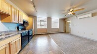 Located at 2195 W State St in Milwaukee, Wisconsin, this one-bedroom, one-bathroom unit offers a well-organized and functional layout across a single floor. The open-concept living and kitchen area creates a spacious feel, with tile flooring in the kitchen transitioning to carpet in the living space. The kitchen is well-equipped with light maple cabinetry, granite-style countertops, black appliances including a refrigerator, stove, and built-in microwave, all illuminated by a track lighting system overhead. The living area benefits from a ceiling fan with integrated lighting and a wall-mounted air conditioning unit, providing year-round comfort. Distinctive glass block windows line the living area walls, allowing diffused natural light to fill the room while maintaining privacy. Baseboard heating runs along the perimeter for added warmth. The bedroom features soft carpeting, a ceiling fan, a built-in closet with shelving, and its own glass block window with blinds. The bathroom includes tile flooring, a wood-paneled vanity with a modern faucet, and accessibility-friendly grab bars. This unit offers a clean, practical living environment with consistent finishes throughout.