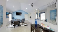 This single-floor professional space is thoughtfully designed to balance functionality with a warm, inviting atmosphere. The reception area greets visitors with light wood-look tile flooring, recessed lighting, and tasteful abstract wall art in shades of blue and gold. Dark espresso-toned cabinetry and filing units provide practical storage while adding a polished, professional touch. A patterned area rug anchors the space and adds visual interest underfoot.

Beyond the reception, a hallway leads into a striking meeting or lounge room distinguished by soaring vaulted ceilings that create a sense of openness and grandeur. This room features a bold sky-blue accent wall that serves as a vibrant focal point, complemented by a wall-mounted flat-screen television. Comfortable upholstered chairs in coordinating patterned fabric surround a round table, making the space well-suited for meetings or collaborative gatherings. Natural light filters in through a window dressed with patterned valances, brightening the room further.

Throughout, the consistent use of blue tones, light flooring, and clean white walls creates a cohesive and professional aesthetic. The thoughtful layout and design details make this space both functional and visually appealing for staff and visitors alike.