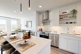 This well-appointed one-bedroom, one-bathroom residence in Waltham, MA offers a thoughtfully designed open-concept layout with modern finishes throughout. The combined kitchen and living area serves as the heart of the home, featuring light wood-style flooring, recessed lighting, and sleek pendant lights over a generous quartz-topped island with seating. The kitchen is outfitted with white flat-panel cabinetry, open shelving, white subway tile backsplash, a stainless steel range with wall-mounted hood, dishwasher, and a French door refrigerator. The living area is bathed in natural light from large windows that frame sweeping views of the surrounding landscape, creating a bright and airy atmosphere. The bedroom offers plush carpeting, two large windows with the same scenic views, and access to a dedicated closet. The bathroom features a wide single-sink vanity with white cabinetry, wood-look flooring, a glass-enclosed walk-in shower with tile surround, and built-in open shelving for added storage. Clean lines, a neutral palette, and contemporary finishes give the entire residence a cohesive and modern character.