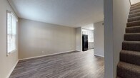 This two-story residence features a straightforward, functional layout with consistent neutral tones and modern updates throughout. The main level opens into a spacious living area finished with durable wood-look plank flooring and neutral gray walls, creating a clean and versatile backdrop. Natural light filters in through a window near the front entry, which features a classic paneled door. The living space flows directly into the kitchen, which is equipped with gray shaker-style cabinetry, light stone-look countertops, a white subway tile backsplash, and a full suite of black appliances including a refrigerator, range, microwave, and dishwasher. The kitchen benefits from additional overhead lighting and angled upper cabinetry that adds visual interest. A bathroom on the main level includes a marble-look countertop and wood-look flooring. Upstairs, the bedrooms are carpeted and generously sized, each featuring ceiling fans with integrated lighting. One bedroom includes a sliding glass door that provides outdoor access and additional natural light, while another features a walk-in closet. A full bathroom upstairs includes a soaking tub with a built-in surround and integrated shelving. The textured ceilings are consistent throughout, and the overall ambiance is clean, move-in ready, and well-maintained.