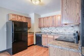 Located at 1518 N Peach Ave in Marshfield, Wisconsin, this one-bedroom, one-bathroom unit offers a practical and efficient single-floor layout. The kitchen is a standout feature, showcasing warm oak cabinetry, granite-style countertops, a tile backsplash, and hardwood flooring. Black appliances — including a refrigerator, range, and dishwasher — are included, providing a fully equipped cooking space with ample storage. The bedroom offers a comfortable, carpeted retreat with a ceiling fan, a window for natural light, and a closet for storage. The neutral-toned walls and plush carpeting create a calm, livable atmosphere. A hallway connects the main living areas and leads to the bathroom, which features a tub/shower combo, hardwood-style flooring, a wood-cabinet vanity with a granite-style countertop, and an overhead storage cabinet. The bathroom's dark wood trim is consistent with the design details found throughout the unit. The overall aesthetic is clean and functional, with warm wood tones, neutral walls, and durable finishes that provide a cohesive look from room to room. This unit is well-suited for those seeking a low-maintenance, efficiently organized living space in a residential Marshfield neighborhood.