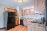 Located at 1518 N Peach Ave in Marshfield, Wisconsin, this one-bedroom, one-bathroom unit offers a practical and efficient single-floor layout. The kitchen is a standout feature, showcasing warm oak cabinetry, granite-style countertops, a tile backsplash, and hardwood flooring. Black appliances — including a refrigerator, range, and dishwasher — are included, providing a fully equipped cooking space with ample storage. The bedroom offers a comfortable, carpeted retreat with a ceiling fan, a window for natural light, and a closet for storage. The neutral-toned walls and plush carpeting create a calm, livable atmosphere. A hallway connects the main living areas and leads to the bathroom, which features a tub/shower combo, hardwood-style flooring, a wood-cabinet vanity with a granite-style countertop, and an overhead storage cabinet. The bathroom's dark wood trim is consistent with the design details found throughout the unit. The overall aesthetic is clean and functional, with warm wood tones, neutral walls, and durable finishes that provide a cohesive look from room to room. This unit is well-suited for those seeking a low-maintenance, efficiently organized living space in a residential Marshfield neighborhood.
