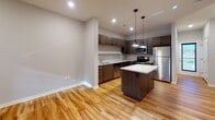 This well-appointed two-story residence showcases a thoughtfully designed interior with a clean, contemporary aesthetic throughout. The main level centers around an open-concept kitchen that serves as a functional hub of the home. The kitchen is outfitted with rich dark-toned cabinetry, light granite-style countertops, a subway tile backsplash, and a full suite of stainless steel appliances including a range, over-the-range microwave, and refrigerator. A central island with pendant lighting above provides additional prep space and casual dining potential. Warm hardwood flooring extends across the main living areas, contributing to an inviting and cohesive feel.

The upper level features carpeted bedrooms that offer a comfortable, quieter retreat. The rooms are generously proportioned with tall ceilings and ample natural light streaming through horizontal windows. Bathrooms are finished with granite-topped vanities, warm wood cabinetry, and full tub-shower combinations. A standout feature is the primary bathroom, which includes a dual-sink vanity with extensive countertop space and connects to an in-unit stacked washer and dryer — offering exceptional convenience. The neutral gray and white palette used throughout the space creates a calm, move-in-ready environment with a polished, modern character.