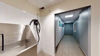 Located at 160 Morgan St in Jersey City, NJ, this single-floor commercial space is purpose-built for pet grooming services. The facility is organized into two distinct areas that work together to create a functional and visually engaging environment.

The main corridor is the centerpiece of the space, featuring a striking decorative wall treatment with a geometric brick-patterned design in grey and white tones. Slate-blue accent walls run along the opposite side, and large-format porcelain tile flooring in a warm beige tone extends throughout. A suspended drop ceiling with recessed skylight-style panels provides consistent, even illumination across the length of the hallway. Framed photographs of dogs are displayed along the patterned wall, reinforcing the pet-focused nature of the business. A pass-through window built into the corridor wall allows for visibility and communication between areas.

The secondary room serves as a dedicated washing and grooming station, finished with clean white subway tile walls and equipped with a deep stainless steel utility sink. A wall-mounted professional grooming dryer with a flexible hose is installed for immediate use. A split-unit air conditioning system is also present, ensuring climate control throughout the space. Together, these two areas form a well-appointed, hygienic, and welcoming grooming facility suited for professional pet care services.