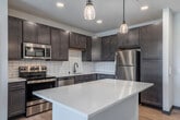 This thoughtfully designed 2-bedroom, 2-bathroom residence is laid out entirely on a single floor, offering a comfortable and functional living environment. The open-concept kitchen and living area serves as the heart of the home, featuring rich dark wood cabinetry, a white subway tile backsplash, stainless steel appliances, recessed lighting, and a generous center island with a clean white countertop illuminated by pendant lights — ideal for both meal prep and casual dining. Light wood-tone flooring flows throughout the main living areas, adding warmth and cohesion to the space.

The primary bedroom is a well-proportioned retreat equipped with a ceiling fan, large windows that invite natural light and outdoor views, and plush carpeting underfoot. The second bedroom also features carpeted floors, a ceiling fan, and a horizontal clerestory window. Each bedroom is paired with its own closet for dedicated storage.

Both bathrooms are finished in a clean, modern style. The primary bath includes dark wood vanity cabinetry, a quartz countertop, a framed mirror, and a glass-enclosed walk-in shower. The second bathroom mirrors this refined aesthetic with a tub-shower combo and light hardwood flooring. Together, these spaces reflect a cohesive, contemporary design throughout.