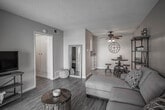 Located at 10381 S Lynn Cir in Jurupa Valley, CA, this single-floor home offers a thoughtfully laid-out living space with warm, inviting interiors throughout. The living room serves as the heart of the home, featuring wood-look flooring, soft yellow-toned walls, and a textured ceiling with a ceiling fan. A sliding glass door opens directly to an outdoor patio, filling the space with natural light and providing easy access to the exterior. The open layout connects the living area to a compact dining space, creating a seamless flow for everyday living. The kitchen is well-equipped, showcasing white cabinetry, granite-style countertops, a double-basin sink, and stainless steel appliances, all set against the same light wood-look flooring that runs throughout the home. The bedroom is a comfortable retreat with a window that brings in natural light, complemented by the consistent warm color palette and wood-look flooring. The bathroom is functional and clean, featuring a white vanity with storage, a mirrored medicine cabinet, a shower-tub combination, and warm lighting above. Overall, this home presents a cohesive, cozy aesthetic with practical finishes and a welcoming atmosphere throughout every room.