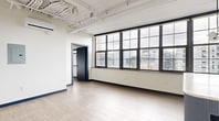 Located at 401 E State St in downtown Ithaca, NY, this one-bedroom, one-bathroom unit showcases a contemporary industrial-loft design characterized by exposed structural beams, soaring ceilings, and light hardwood flooring throughout. The open living area is defined by a sweeping bank of large, black-framed grid windows that flood the space with natural light and frame elevated views of the surrounding cityscape.

The kitchen is a standout feature, equipped with slate-blue cabinetry, granite countertops, a tile backsplash, stainless steel appliances including a refrigerator, dishwasher, and microwave, and a deep undermount sink. A fluted-panel kitchen island with a white quartz top anchors the space and serves as a natural divider between the kitchen and living area. Pendant globe lighting adds a modern, curated touch overhead.

The bedroom is a well-proportioned private retreat with its own set of black-framed windows overlooking the city, hardwood flooring, and bold navy baseboards that complement the unit's consistent design language. A dedicated closet provides practical storage.

The bathroom features large-format grey tile on both the floors and walls, a blue vanity, and clean, minimalist fixtures. The unit's cohesive palette of white, grey, and navy blue creates a polished, contemporary ambiance throughout.