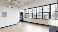 Located at 401 E State St in downtown Ithaca, NY, this one-bedroom, one-bathroom unit showcases a contemporary industrial-loft design characterized by exposed structural beams, soaring ceilings, and light hardwood flooring throughout. The open living area is defined by a sweeping bank of large, black-framed grid windows that flood the space with natural light and frame elevated views of the surrounding cityscape.

The kitchen is a standout feature, equipped with slate-blue cabinetry, granite countertops, a tile backsplash, stainless steel appliances including a refrigerator, dishwasher, and microwave, and a deep undermount sink. A fluted-panel kitchen island with a white quartz top anchors the space and serves as a natural divider between the kitchen and living area. Pendant globe lighting adds a modern, curated touch overhead.

The bedroom is a well-proportioned private retreat with its own set of black-framed windows overlooking the city, hardwood flooring, and bold navy baseboards that complement the unit's consistent design language. A dedicated closet provides practical storage.

The bathroom features large-format grey tile on both the floors and walls, a blue vanity, and clean, minimalist fixtures. The unit's cohesive palette of white, grey, and navy blue creates a polished, contemporary ambiance throughout.