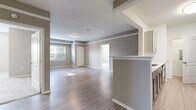This single-floor, 2-bedroom, 2-bathroom residence in Eden Prairie, Minnesota offers a thoughtfully designed layout with modern finishes throughout. The open-concept living and dining area is bathed in natural light, featuring smooth hardwood-style flooring, neutral gray walls, crown molding, and a ceiling fan — creating a bright and welcoming atmosphere. A kitchen bar counter provides a seamless transition into the well-equipped galley kitchen, which boasts gray shaker-style cabinetry, white quartz countertops, stainless steel appliances including a refrigerator and dishwasher, and light wood-tone flooring. The spacious primary bedroom offers plush carpeting, generous wall space, and a ceiling fan, while the second bedroom also features soft carpet and a large window overlooking lush outdoor greenery. The bathrooms are finished with elegant white quartz vanity countertops, undermount sinks, gray cabinetry, and brushed nickel fixtures, complemented by a clean soaking tub and tiled surround. A dedicated laundry area and closet add everyday convenience. The overall design palette of soft grays, whites, and warm wood tones gives this residence a cohesive, contemporary feel.