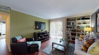 This single-story residence offers a well-organized layout that balances comfort and functionality across several distinct living areas. The living room serves as the heart of the home, showcasing warm hardwood-style flooring, a textured ceiling, and bold accent walls in olive green and slate blue. Built-in shelving provides ample display space, while a large sliding glass door floods the room with natural light and opens to an outdoor balcony area. An adjacent dining area features rich hardwood-style flooring, crown molding, a warm amber accent wall, and a pendant light fixture overhead, creating an intimate setting for meals.

The galley-style kitchen is efficiently designed with white cabinetry lining both sides, dark granite-style countertops, black appliances including a refrigerator, dishwasher, and range, and a double sink. Tile flooring runs throughout this space, adding a clean, practical finish.

The bedroom features plush carpet, a ceiling fan with light fixture, a bold teal accent wall, and generous window coverage with striped drapery that allows for natural light control. Two full bathrooms each offer a tub-shower combination with tile surrounds, white cabinetry, and tile flooring, providing practical and well-appointed spaces.