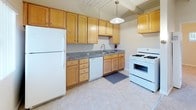 This single-floor residence offers a well-organized layout with a variety of practical and comfortable spaces. The kitchen is a standout feature, equipped with warm honey-toned wood cabinetry, granite countertops, and white appliances including a gas range, dishwasher, and refrigerator. Tile flooring and a pendant light fixture overhead add a functional, clean aesthetic to the space. A window above the sink allows for natural light to filter in.

The carpeted rooms provide a soft, comfortable feel underfoot and are bathed in natural light through horizontal strip windows near the ceiling, giving a sense of openness while maintaining privacy. Exposed wooden beam ceilings with a plank inlay add architectural character throughout, complemented by ceiling fans that enhance comfort.

The bathroom is clean and classic, featuring white subway-style wall tiles surrounding a full tub-shower combination, a single-basin vanity with chrome fixtures, and a window that allows for natural ventilation and light. The overall palette throughout the home is neutral and bright, with white walls and light-toned finishes that create an airy, welcoming ambiance. The floor plan, as seen in the dollhouse view, reveals a compact yet efficient arrangement of interconnected rooms suited for comfortable everyday living.