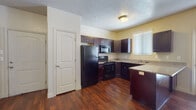 This single-story residence is designed with a functional and cohesive aesthetic throughout. The kitchen serves as a central highlight, featuring dark espresso cabinetry paired with granite-style countertops and a suite of black appliances, including a refrigerator, range, built-in microwave, and dishwasher. Rich hardwood-style flooring runs through the kitchen, complemented by natural light from a window fitted with blinds. Ample upper and lower cabinet storage provides substantial organization options.

The bedrooms offer plush wall-to-wall carpeting and individual windows with blinds, creating bright, comfortable spaces. One bedroom includes access to a generously sized walk-in closet outfitted with multiple shelving units and hanging rods along two walls.

Two full bathrooms mirror each other in style, each featuring dark espresso vanities with granite-style countertops, stone-look tile flooring, large mirrors, and a tub-shower combination with a white surround. Brushed nickel fixtures and hardware add a refined finishing touch.

A dedicated laundry area accommodates a full-sized side-by-side washer and dryer with overhead shelving for added storage. Textured ceilings are present throughout, contributing to the overall character of the space.