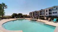 The outdoor pool area offers a well-appointed recreational retreat designed for relaxation and leisure. The centerpiece is a generously sized swimming pool with clear, blue-green water, complemented by a circular spa positioned directly adjacent, finished with decorative tile detailing. Entry to both the pool and spa is made convenient through multiple stainless steel handrails and step entries.

Surrounding the water features is an expansive concrete sun deck furnished with lounge chairs and small accent tables, providing ample space for sunbathing and outdoor socializing. The area is enclosed by a wrought iron fence, offering both security and an open, airy feel. Neatly trimmed hedges and ornamental shrubs line the perimeter, adding a touch of greenery to the hardscape environment.

The pool area benefits from open sky exposure, allowing for abundant natural sunlight throughout the day. The backdrop includes a multi-story residential building with balconies overlooking the amenity space, and mature trees visible beyond the fence line provide a natural visual boundary. Overall, the space presents a clean, well-maintained atmosphere suited for outdoor recreation.