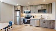 Located at 2024 Jane St in Pittsburgh's South Side neighborhood, this one-bedroom, one-bathroom unit offers a thoughtfully designed layout across a single floor. Light wood-tone flooring runs throughout, lending warmth and visual continuity to the entire space.

The kitchen is a standout feature, outfitted with floor-to-ceiling wood-grain cabinetry accented by matte black hardware, white quartz countertops, and a full suite of stainless steel appliances including a refrigerator, range, over-the-range microwave, and dishwasher. A window at the end of the galley-style kitchen draws in natural light and frames a charming Pittsburgh cityscape, complemented by a compact dining area.

The bedroom is generously proportioned, offering ample room for a full sleeping and living arrangement. A large window provides scenic views of the surrounding Pittsburgh neighborhood, while recessed lighting and a wall-mounted TV add modern convenience. A dedicated workspace with a desk is also incorporated into the room.

The bathroom is clean and contemporary, featuring a wood-grain vanity with a white countertop, an LED-backlit mirror, and a sliding glass walk-in shower with dark hardware accents. The overall design of this unit reflects a cohesive modern aesthetic with practical, well-appointed finishes throughout.