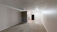 Located at 1600 Jones Dr in Arlington, TX, this one-bedroom, one-bathroom unit offers a practical and well-organized single-floor layout. The living room features neutral-toned carpet, a textured ceiling, and a two-tone wall design with a darker accent wall, creating a subtle visual contrast. Wood-look flooring transitions into the kitchen area, which includes white cabinetry, a breakfast bar, and a black appliance package, as visible in the dollhouse overview. The spacious bedroom is carpeted and features a ceiling fan with integrated lighting and a window fitted with blinds that allows for natural light. The room offers ample space for standard bedroom furnishings. The full bathroom is clean and functional, equipped with a tiled shower-tub combo, chrome fixtures, a toilet, and a vanity with a granite-style countertop and wood-look flooring. A hallway connects the main living areas and provides access to a closet for additional storage. Throughout the unit, neutral wall colors, textured ceilings, and consistent flooring choices contribute to a cohesive and understated aesthetic suited for comfortable everyday living.