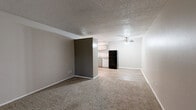 Located at 1600 Jones Dr in Arlington, TX, this one-bedroom, one-bathroom unit offers a practical and well-organized single-floor layout. The living room features neutral-toned carpet, a textured ceiling, and a two-tone wall design with a darker accent wall, creating a subtle visual contrast. Wood-look flooring transitions into the kitchen area, which includes white cabinetry, a breakfast bar, and a black appliance package, as visible in the dollhouse overview. The spacious bedroom is carpeted and features a ceiling fan with integrated lighting and a window fitted with blinds that allows for natural light. The room offers ample space for standard bedroom furnishings. The full bathroom is clean and functional, equipped with a tiled shower-tub combo, chrome fixtures, a toilet, and a vanity with a granite-style countertop and wood-look flooring. A hallway connects the main living areas and provides access to a closet for additional storage. Throughout the unit, neutral wall colors, textured ceilings, and consistent flooring choices contribute to a cohesive and understated aesthetic suited for comfortable everyday living.