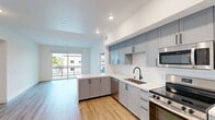 This well-designed 2-bedroom, 2-bathroom unit at 850 N Azusa Ave offers a clean, contemporary aesthetic throughout its efficiently laid-out single floor. The open-concept kitchen flows seamlessly into the living area and is appointed with gray shaker-style cabinetry, white quartz countertops, a white subway tile backsplash, a stainless steel undermount sink with a matte black faucet, and a full suite of stainless steel appliances including a gas range, over-the-range microwave, dishwasher, and refrigerator. A peninsula countertop extends the workspace and provides additional seating. Light wood-style flooring runs throughout the unit, lending warmth and visual continuity across all spaces. The living area receives generous natural light and offers direct access to a private balcony with outdoor views. Both bedrooms are bright and well-proportioned, each featuring windows that bring in natural light. The primary bedroom includes access to a dedicated closet. The bathrooms maintain the unit's modern design with gray vanity cabinetry, illuminated mirrors, white countertops, and a tub-shower combination. Three closets in total provide ample storage. The unit's neutral white walls and consistent finishes create a bright, move-in-ready environment throughout.