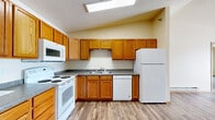 Located at 5001 Amber Valley Pkwy S in Fargo, North Dakota, this single-floor unit offers 2 bedrooms, 3 bathrooms, and a versatile den. The open-concept living and kitchen area is anchored by warm hardwood-style vinyl flooring and a skylight-style ceiling fixture that brightens the space throughout the day. The kitchen is well-equipped with warm oak cabinetry, granite-look countertops, and a full suite of white appliances including a range, dishwasher, refrigerator, and over-the-range microwave. Ample upper and lower cabinet storage makes this kitchen both functional and efficient. The living area flows naturally from the kitchen, offering generous open space with baseboard heating and neutral cream-toned walls. Both bedrooms are carpeted, providing a comfortable feel underfoot, and each features a window with natural light, a closet, and baseboard heating. The primary bathroom is spacious and elongated, featuring oak cabinetry, granite-look countertops, a single vanity, and a full soaking tub. A connecting hallway with hardwood-style flooring ties the rooms together seamlessly. The den provides flexible additional space suitable for a home office or guest room. Textured ceilings and warm wood trim throughout lend a cohesive, classic aesthetic to the entire unit.